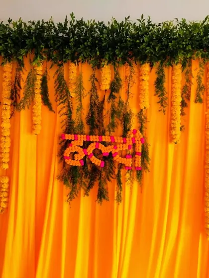A classic Haldi backdrop that radiates pure joy. We used bright yellow drapes as a base, topped with a lush border of green leaves and hanging marigold garlands, with the word 'Haldi' crafted from flowers as the centerpiece.