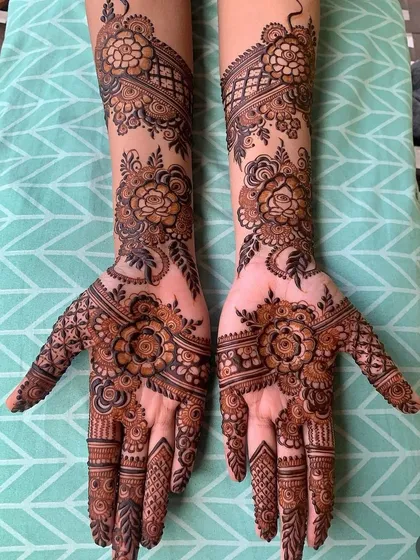 A classic full-hand Arabic style mehndi. This design features beautiful floral patterns connected by flowing vines that extend from the palms to the arms, filled in with detailed checks and shading for a rich, complete look.