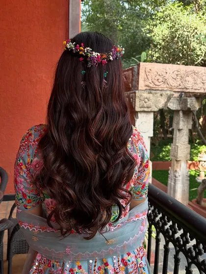 The back of the bride's hair, styled in a half-updo with a crown of fresh, colorful flowers. This bohemian-inspired look is perfect for an outdoor Haldi celebration.