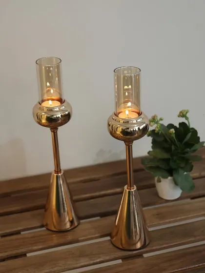 A pair of our tall Vesper candle holders in a polished gold finish. Their sleek, conical base and glass hurricane shades are designed to add height and sophistication to your decor.