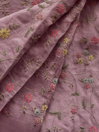 Our embroidered slub silk in a dusty rose shade, featuring delicate multi-color floral threadwork. This fabric has a beautiful texture that adds depth and elegance to any outfit.