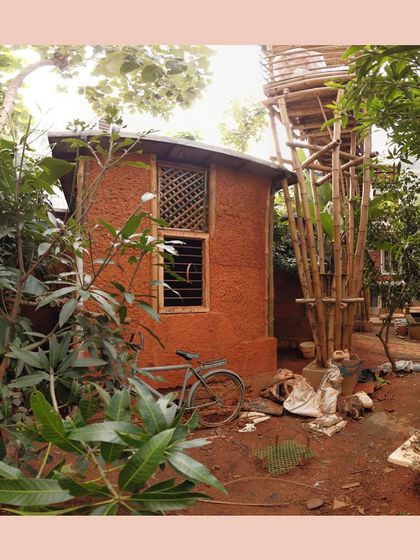 A small cottage built with cob and wattle-and-daub techniques, nestled amongst lush greenery, showcasing a truly organic and rustic approach to architecture.