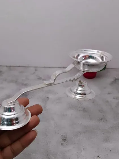 A German silver harathi (aarti lamp) with a long handle, designed for safely performing aarti during pooja.