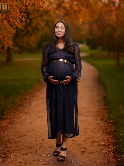 A solo portrait of a mom-to-be walking along a leaf-strewn path in a navy blue gown.