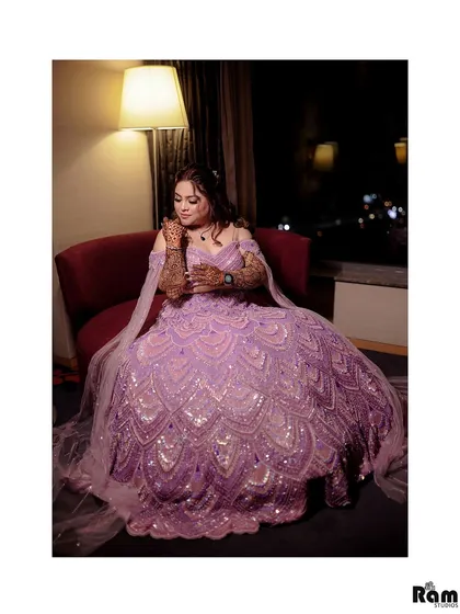 A stunning portrait of the bride-to-be, showcasing her intricate lavender lehenga. The soft lighting from the lamp and the city lights in the window create a beautiful, moody ambiance.