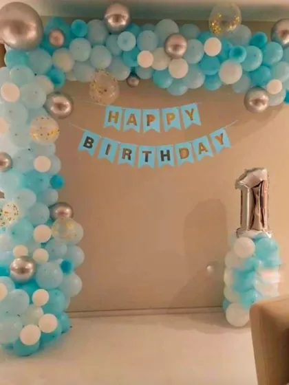 Even a simple corner of your home can be transformed for a birthday celebration. This classic balloon arch in shades of blue and silver, complete with a "Happy Birthday" banner and a number foil balloon, is perfect for an intimate at-home party.