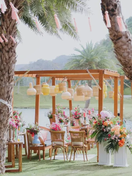 A beautiful seating arrangement by the lake, with hanging cane lamps and tassels in the palm trees, all part of the 'Sunny Sway Soirée'.