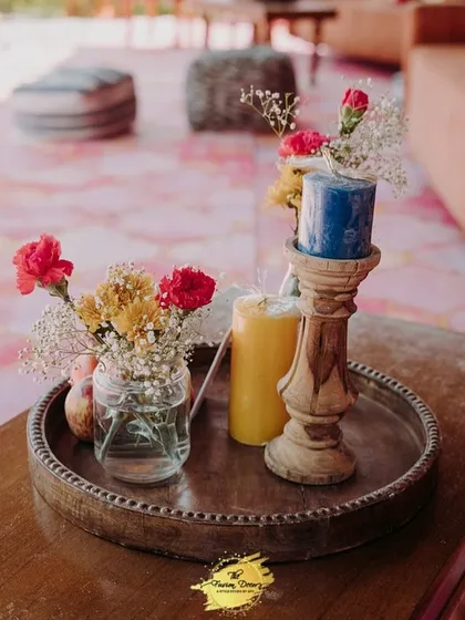 A simple yet beautiful centerpiece for the Haldi lunch. A wooden tray holds colourful candles and small jars of fresh carnations, adding a touch of rustic elegance to the tables.