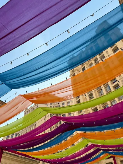 A vibrant canopy of colorful drapes in shades of purple, blue, orange, and pink, creating a festive ceiling for a Mehendi party.