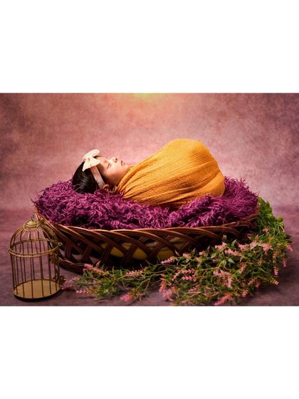 A side view of a newborn sleeping in a basket. The warm lighting and rich purple and mustard tones create a cozy and artistic portrait.