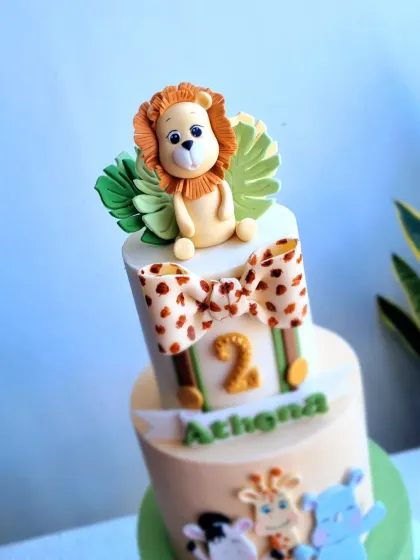 A close-up of the lion topper and giraffe-print bow on the three-tiered safari cake.