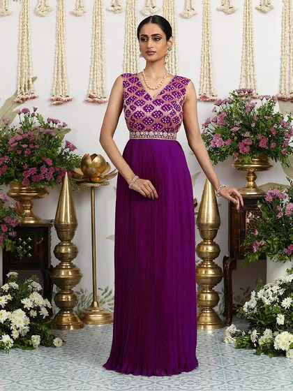 A regal purple pleated gown with a Bandhani-inspired embroidered bodice. The V-neckline and embellished belt add to its sophisticated charm.