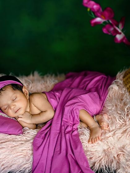 A beautiful composition of a newborn in a hanging basket, with a long purple drape and flowers.