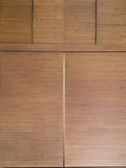 A detail of a fluted wooden wardrobe, showcasing the beauty of precise craftsmanship. The rhythmic texture of the wood adds depth and sensory richness to the space.