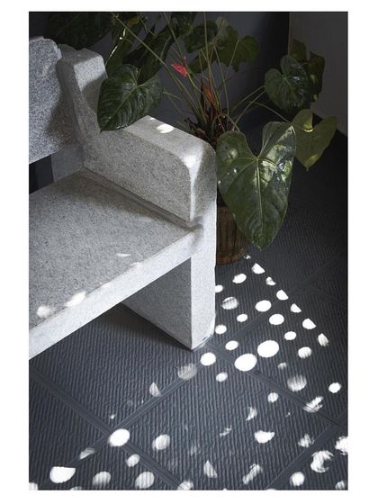A custom-designed stone bench sits in a shower of light from a perforated screen. The robust, monolithic form of the bench contrasts with the ephemeral quality of the light.