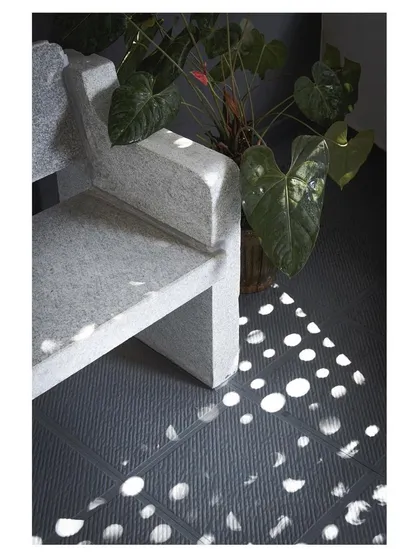 The play of light is a key feature of this home. Here, sunlight passing through a perforated screen creates a beautiful pattern of dots on the floor next to a custom-designed stone bench.