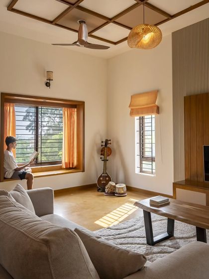 A cozy bay window in the Banashankari living room serves as a perfect reading nook. The Jaisalmer stone flooring and wood-and-cane coffered ceiling enhance the warm, grounded palette of the space.