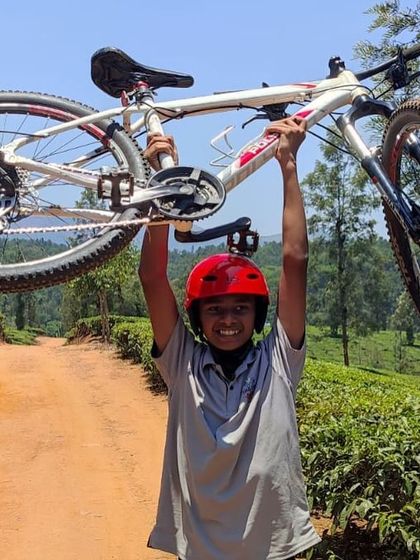 A triumphant camper lifts his mountain bike overhead after completing a challenging ride through the Coorg hills.