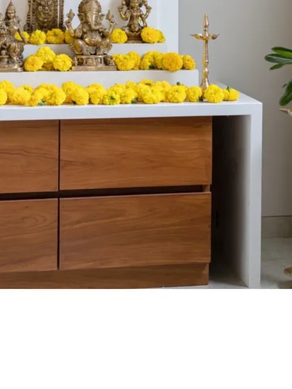 A detail of the mandir storage unit, combining a clean white stone top with warm wood drawers. Fresh marigolds add a traditional and vibrant touch of color.