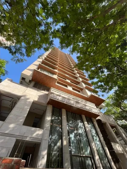 A view from the ground up of the tower under construction, framed by lush greenery. This shot captures the building's impressive scale and the integration of natural elements into the urban design.