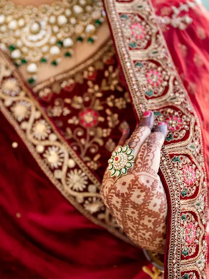 A close up shot focusing on the bride's hand, adorned with intricate mehendi and a statement ring, resting on her rich red lehenga.