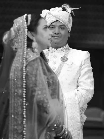 A creative black and white portrait of the bride and groom. The groom is in focus while the bride is in the foreground, creating a sense of depth and story.