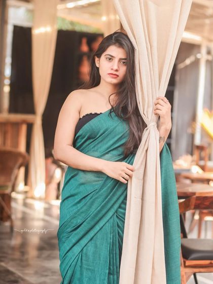 A modern take on saree styling. The model wears a teal saree paired with a contemporary black top, shot in a cafe with earthy tones. This shows how traditional wear can be styled for a modern, chic look.