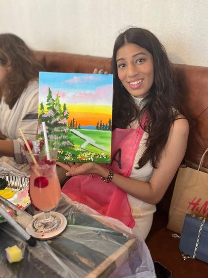 A participant at a wine and paint night, enjoying a drink while she creates her landscape painting. It's the perfect way to unwind.