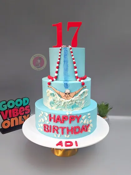A three-tiered swimming themed cake for a champion's 17th birthday. The hand-painted swimmer, water splashes, and lane ropes create a dynamic and celebratory design.
