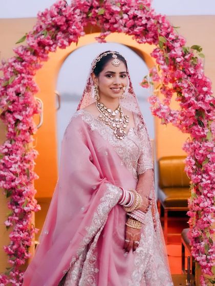 Tanisha looking like a vision in her pastel pink wedding lehenga at Mayfair, Raipur. The makeup is soft and ethereal, with a rosy blush and gentle shimmer on the eyes to complement the delicate color palette of her outfit.