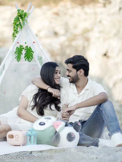 A sweet, candid moment of a couple looking at each other, seated in a picnic setup with a teepee tent.