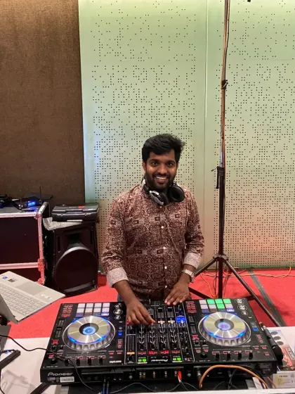 All smiles behind my DJ setup at an indoor hall. My setup is adaptable for different spaces, from large ballrooms to more intimate venues.
