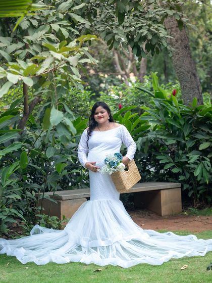A graceful portrait of a mom-to-be in a white mermaid-style gown, standing in a lush green park.