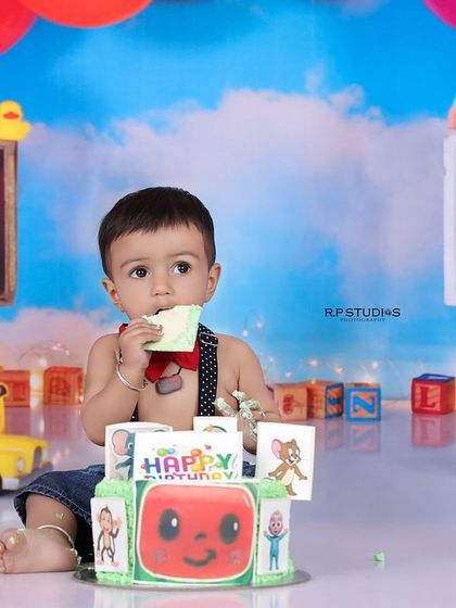 A baby boy gets ready to enjoy his Cocomelon-themed birthday cake. The colorful setup and matching cake make for a fun and memorable cake smash session.