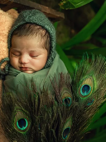A newborn peacefully sleeps, adorned with peacock feathers. This image subtly incorporates elements of the Krishna theme into a classic newborn portrait.