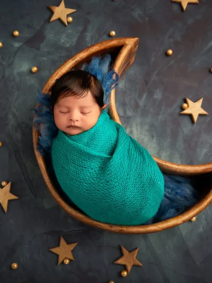 "Love you to the moon and back." This popular theme features a baby sleeping peacefully in a wooden moon prop, set against a starry night backdrop.