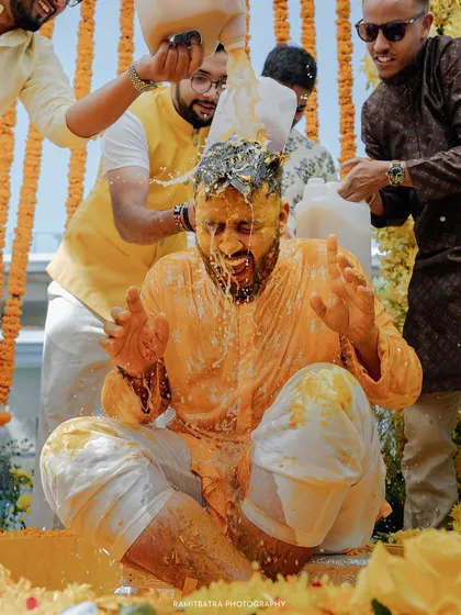 The groom braces himself as his friends pour jugs of milk over him during a joyous and messy Haldi in Thailand.