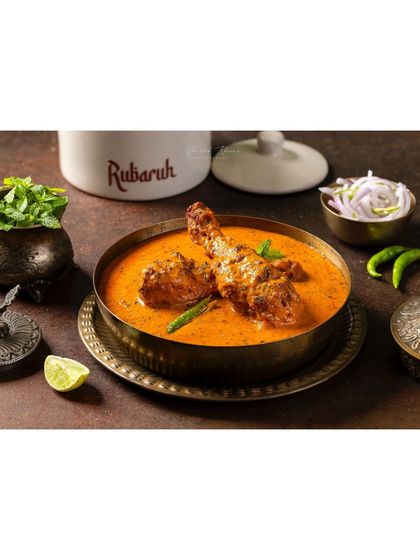 A wide shot of Chicken-e-Rubaruh, showing the dish in context with its branding and serving accompaniments.