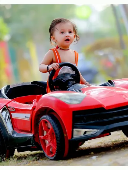 A toddler enjoying a ride in a bright red toy sports car. Outdoor settings provide a dynamic backdrop for our fun vehicle-themed shoots.