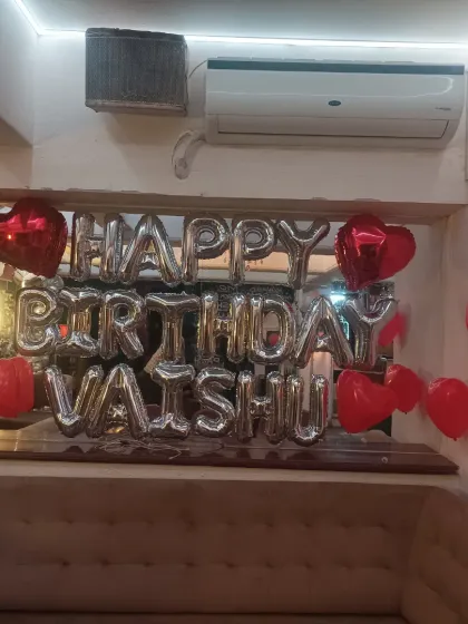 A personalized birthday banner with "Happy Birthday Vaishu" in silver foil letters, surrounded by red heart balloons.