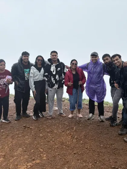 A group of trekkers posing at the summit of Nethravathi, wearing raincoats and jackets to brave the chilly, misty weather.