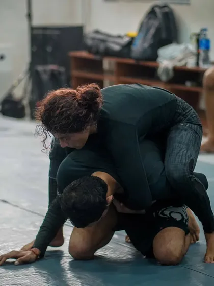 A female student demonstrates a dominant top position in a No-Gi grappling exchange. We focus on teaching techniques that are effective regardless of size or strength.
