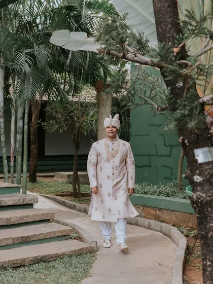 The groom, in his wedding sherwani, walks along a garden path, ready for the ceremony.