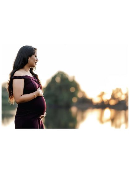 A serene, side-profile portrait of an expectant mother looking out over a lake at sunset. The golden light creates a beautiful, peaceful silhouette.