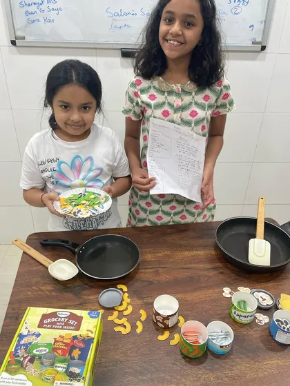 Two students present their final dish from our pretend cooking session. This activity encourages teamwork and gives them a chance to practice explaining their creation to an audience.