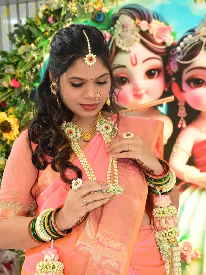 A close-up of a client wearing her baby shower jewellery. This set features a maang tikka, nath (nose ring), necklace, and haath phool made from jasmine buds with red and orange accents.