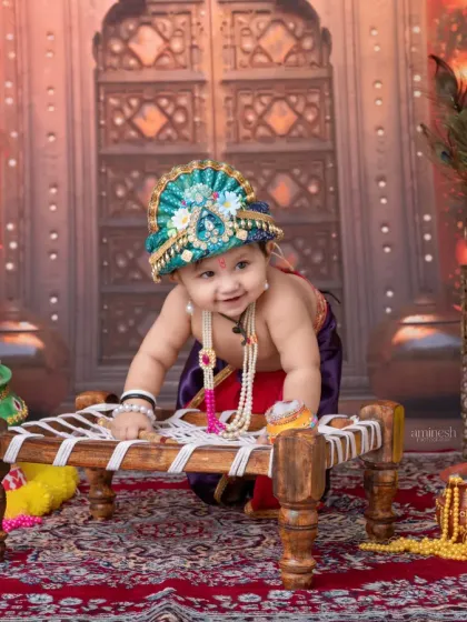 A playful crawling pose from a baby Krishna, interacting with a miniature cot. The setup includes peacock figures and earthen pots, adding layers of detail to the scene.