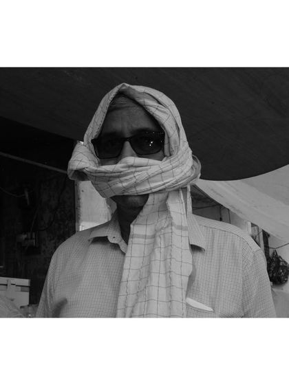 A black and white portrait of a man in Banaras, his face wrapped in a cloth to shield from the sun. The image focuses on his eyes and the texture of the fabric, creating a sense of mystery.