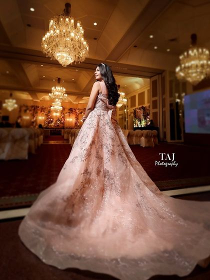A magnificent shot of the bride from the back, showcasing the full glory of her long, flowing reception gown in a grand ballroom.