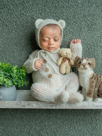 A whimsical portrait of a baby boy sitting on a shelf with his little cat and bear friends. This shows the fun and creative setups we can do.
